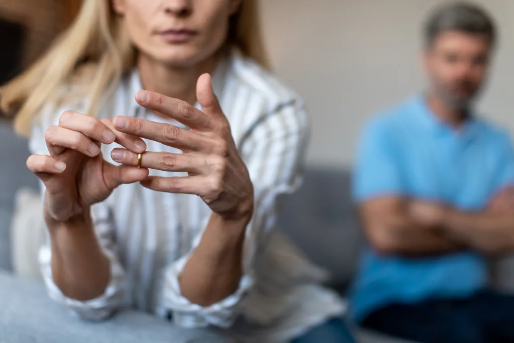 Woman removing her wedding ring during a tense conversation at home while deciding whether she can keep the house after divorce